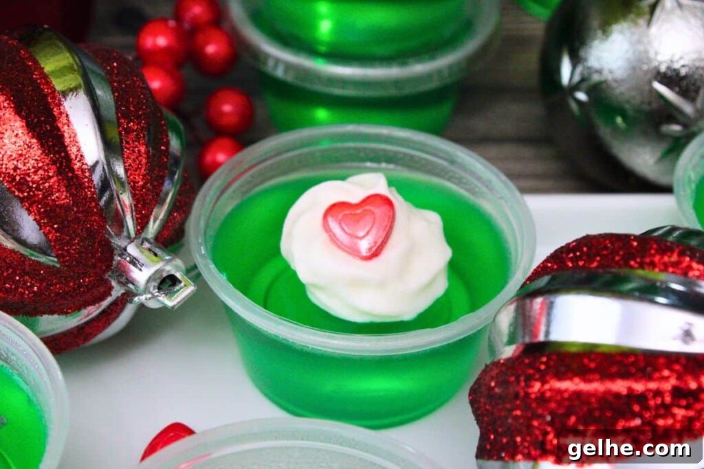 closeup shot of grinch jello shot surrounded by christmas ball ornaments