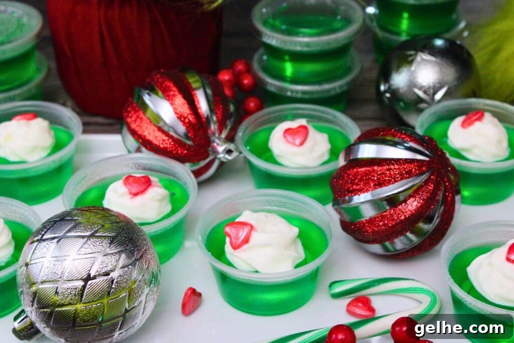 several grinch jello shots on a platter surrounded by christmas ornaments and candy hearts