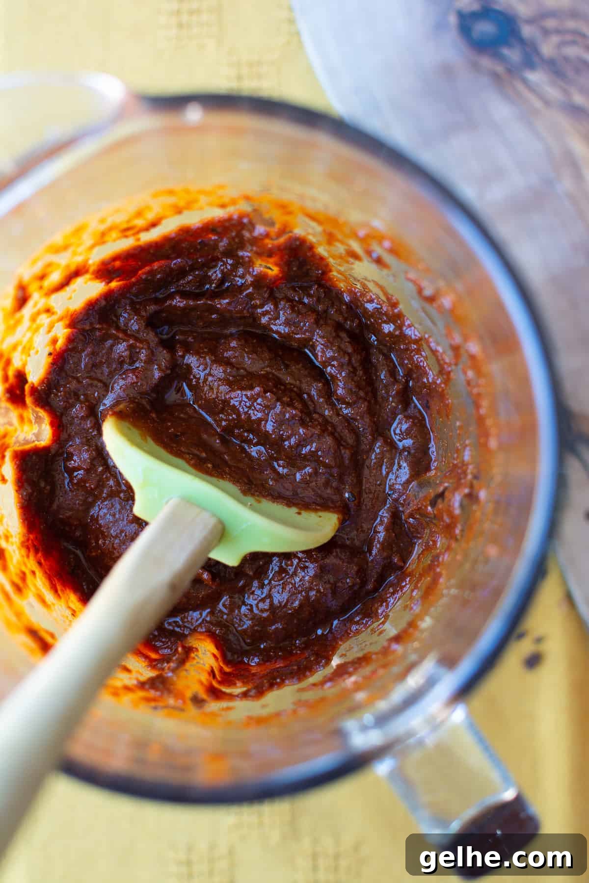 A close up image of chile paste in a blender with a green rubber spatula sticking in the Chile paste.