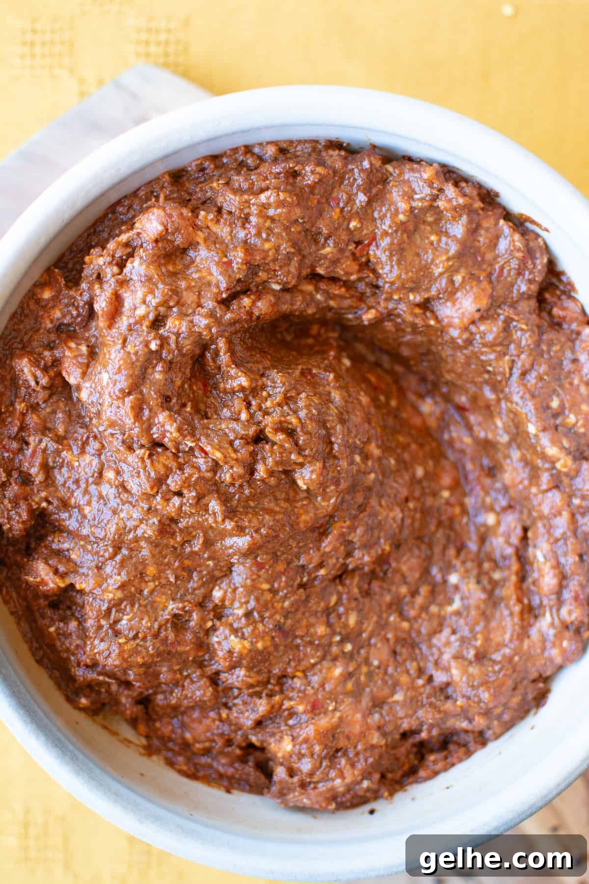 Homemade, uncooked Mexican chorizo in a ceramic bowl sitting on a wood cutting board on a yellow table.