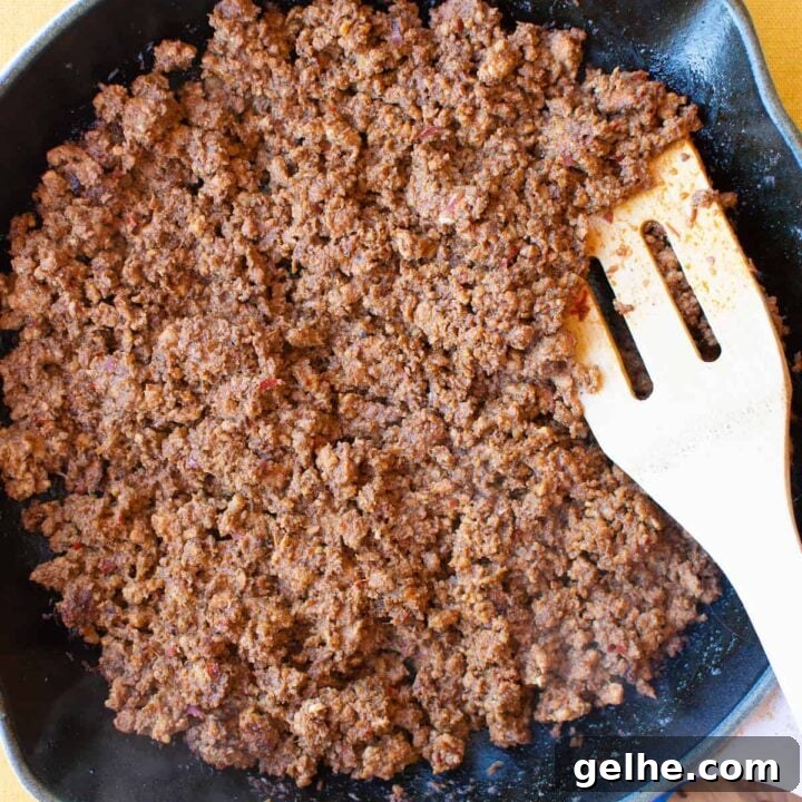 Overhead image of Mexican chorizo cooking in a skillet with a wooden spoon in one side of the pan.