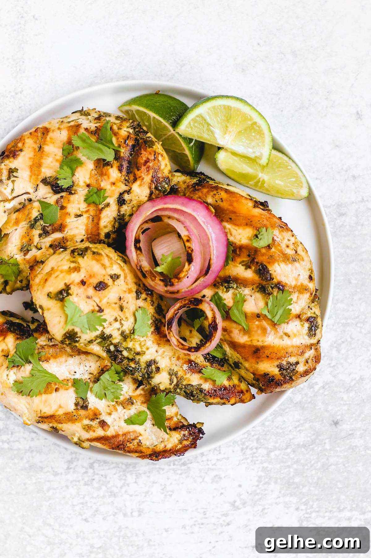 Four grilled cilantro lime chicken breasts with grilled onions and lime slices on a round plate.