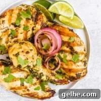 Four grilled cilantro lime chicken breasts with grilled onions and lime slices on a round plate.