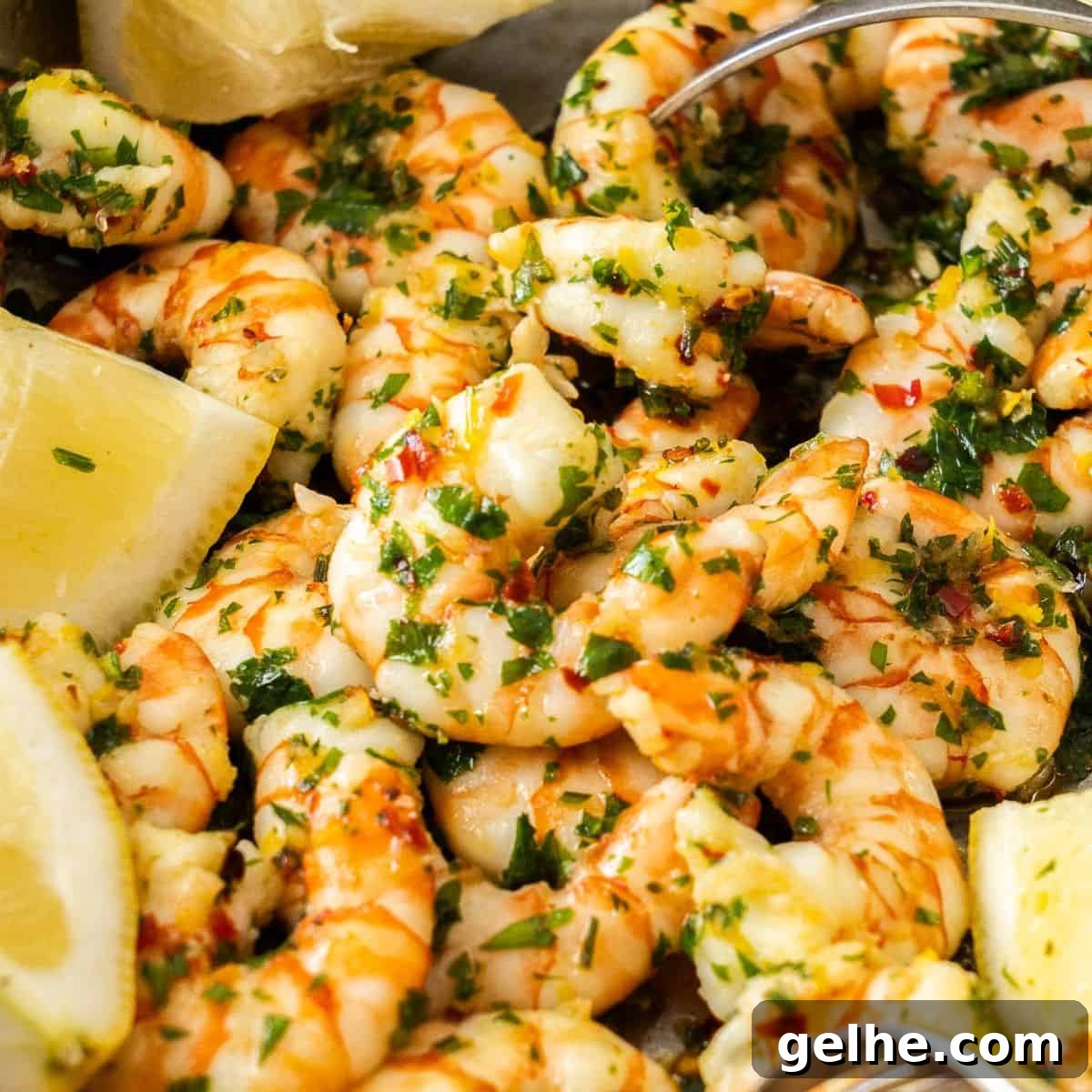 Frying pan with the cooked prawns, served with lemon wedges, two forks in the frying pan reaching for a prawn.