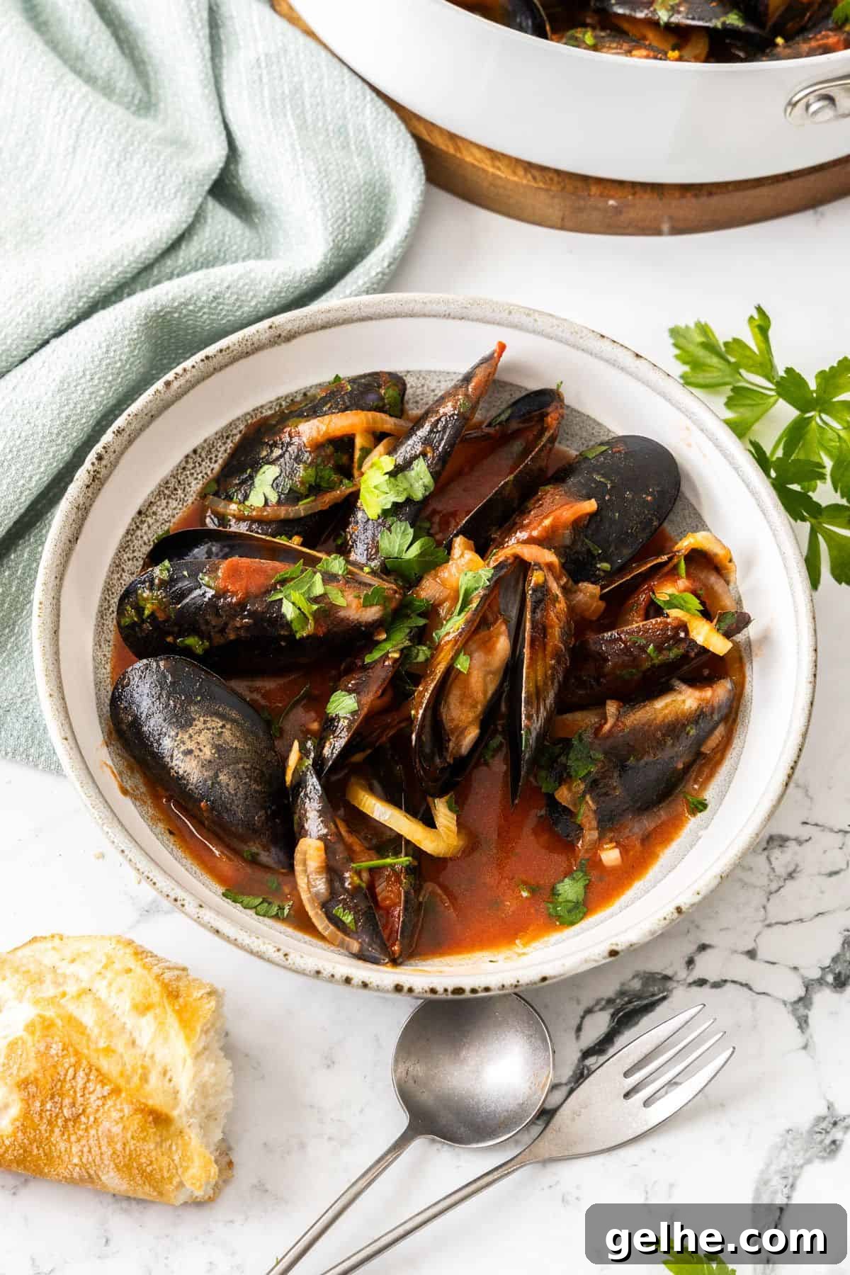 A serving of Mussels in Tomato Sauce, with some bread and cutlery sitting next to the bowl.