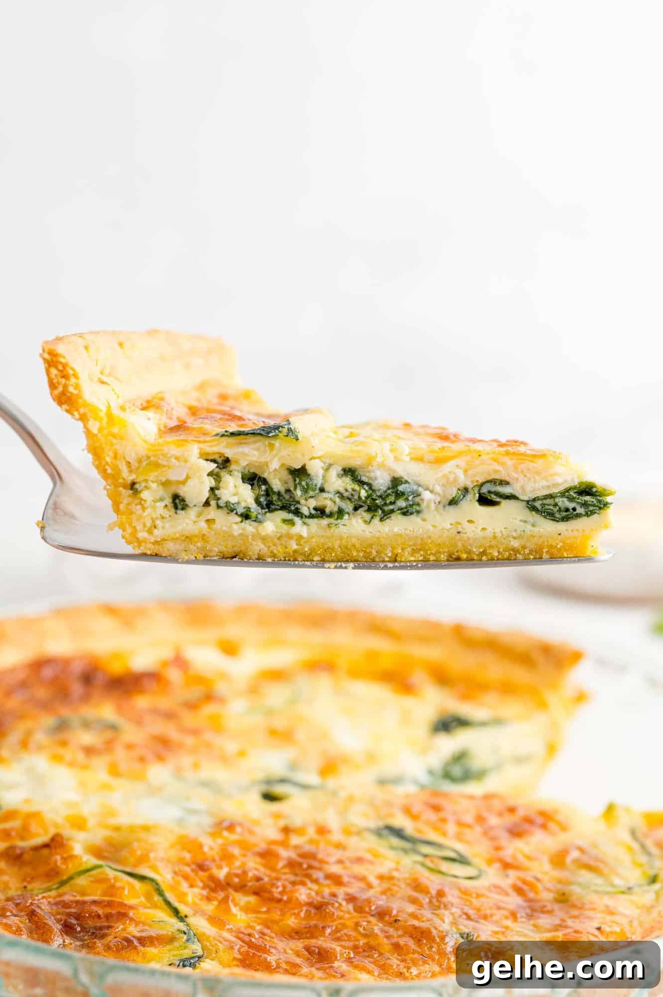 Quiche being served using a pie server, remaining quiche in background.