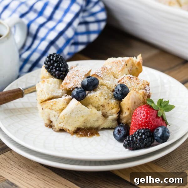 A slice of bread pudding with scattered blackberries and blueberries, alongside a strawberry, on a white plate.
