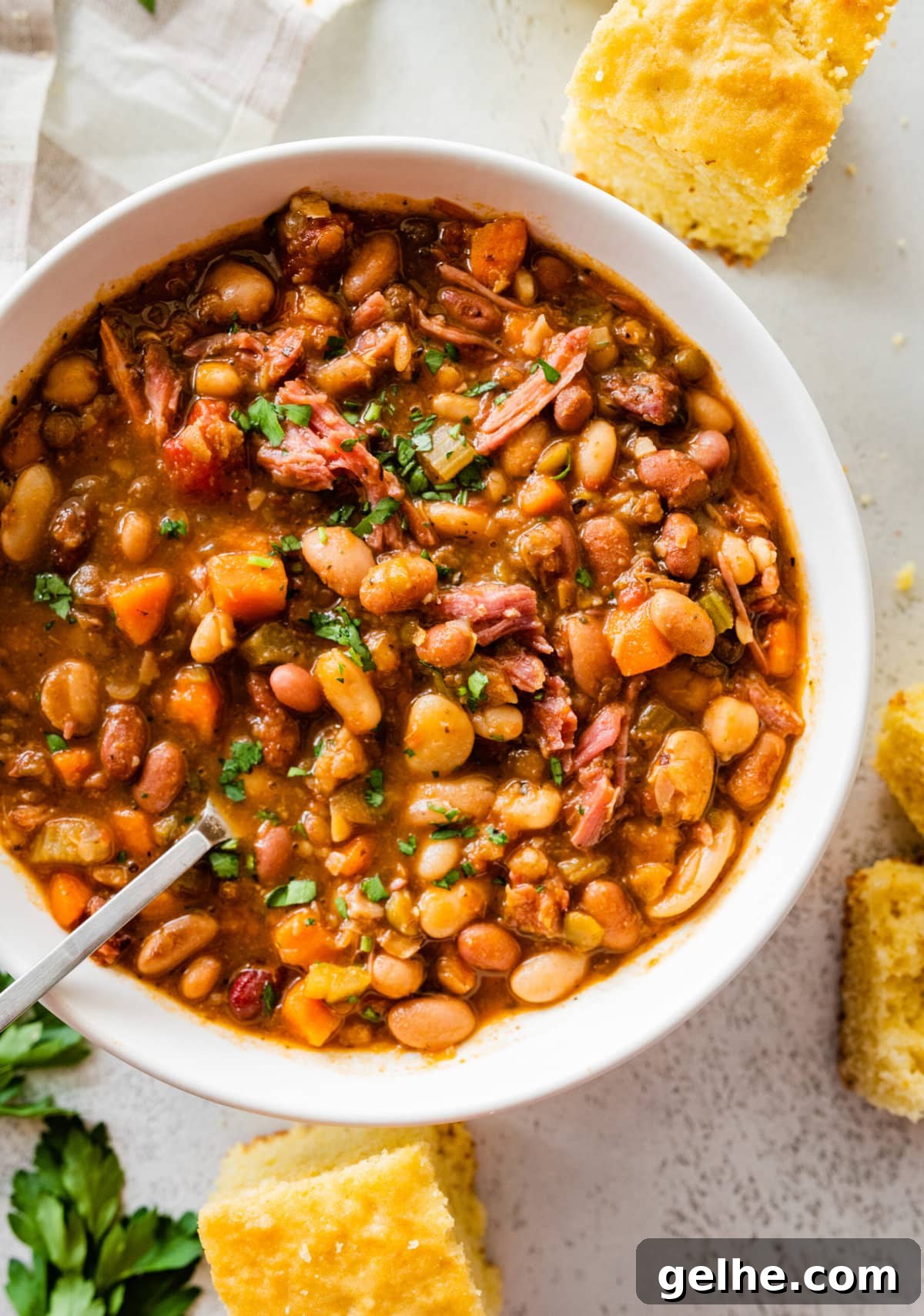 15 bean soup mix recipe in a white bowl with slices of cornbread on the side. Parsley for garnish.