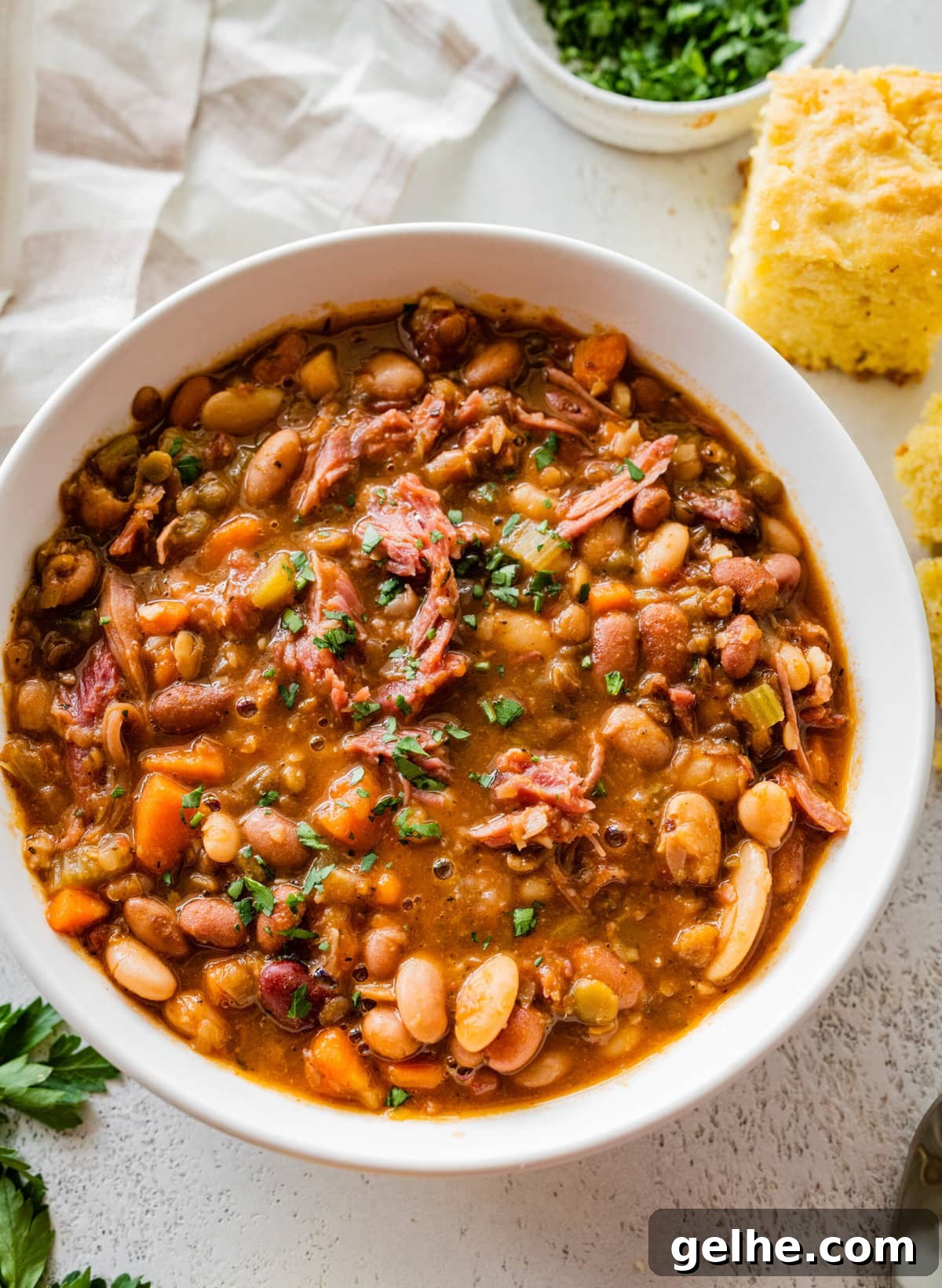 15 bean soup mix recipe in a white bowl with slices of cornbread on the side.