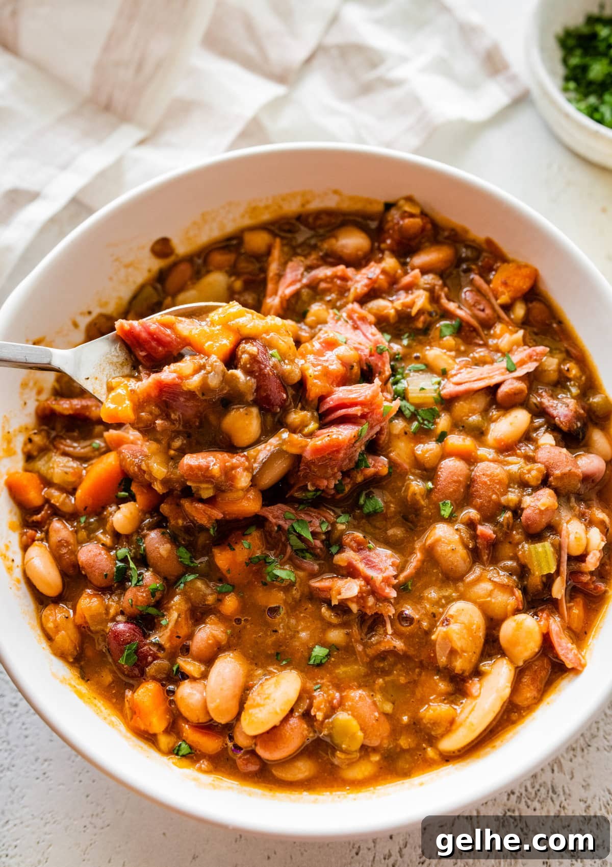 15 bean soup mix recipe in a white bowl with slices of cornbread on the side. spoon in bowl taking a bite of the soup.