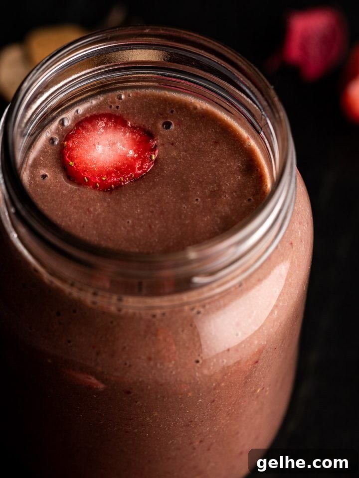 Close up view of a strawberry banana chocolate smoothie in a mason jar, on a black marble board.