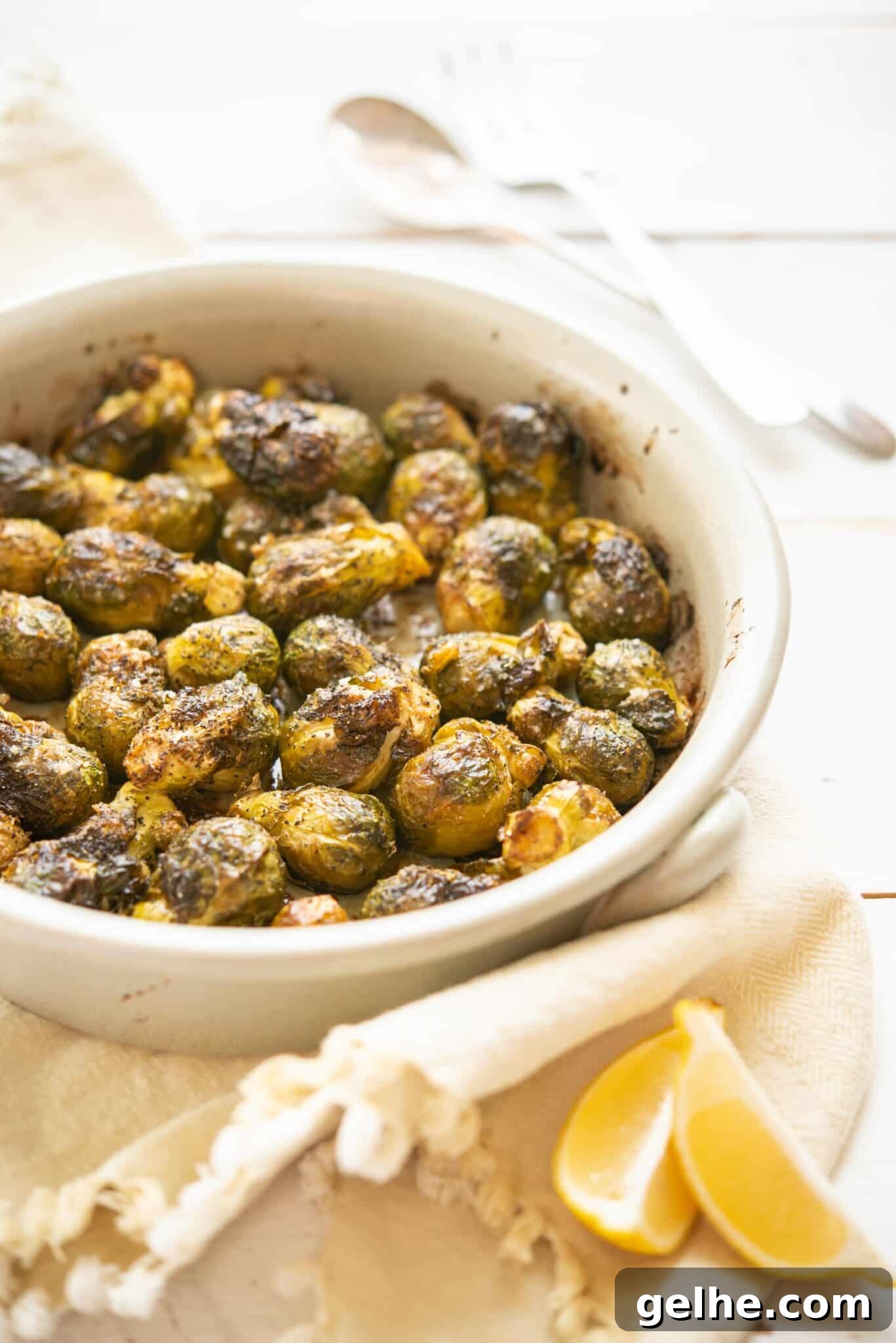 side view of whole roasted brussels sprouts in a round, white ceramic dish on top of a linen towel