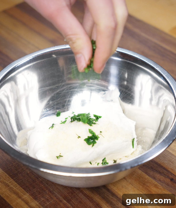 Korean Garlic Cheese Bread Recipe — Crispy, Cheesy Garlic Pull-Apart 4 Parsley is added to a metal bowl of cream cheese, sugar, and parmesan to make the filling for Korean Garlic Cheese Bread.