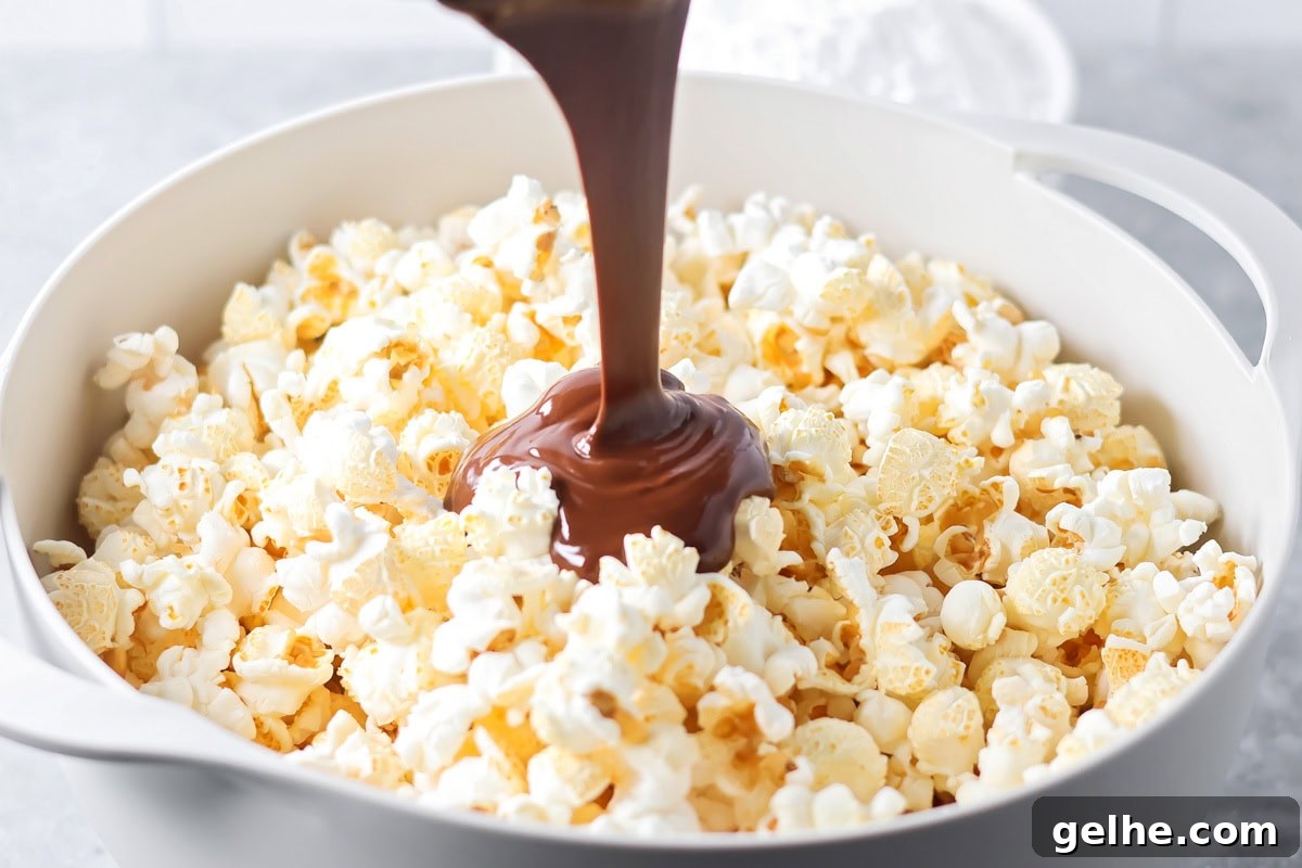 Puppy Chow Popcorn is an irresistible sweet and salty snack that's easy to make and guaranteed to be a hit. Pouring the chocolate peanut butter coating over a bowl of fluffy popcorn.
