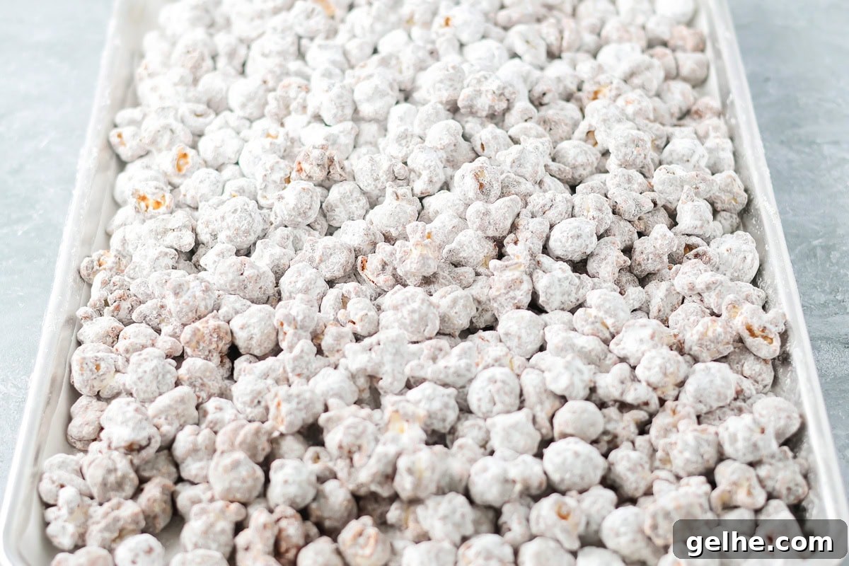 Puppy Chow Popcorn is an irresistible sweet and salty snack that's easy to make and guaranteed to be a hit. Coated puppy chow popcorn spread out to cool on a baking sheet.