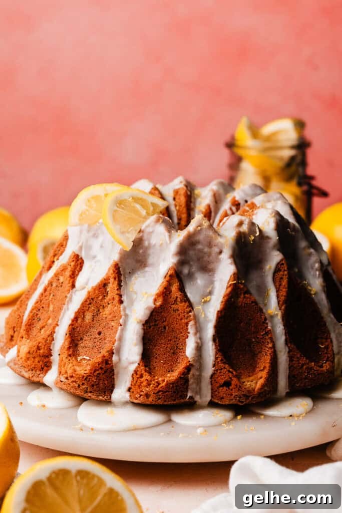 Moist Lemon Poppy Seed Bundt Cake Recipe with Zesty Glaze 11 The glazed bundt cake on a marble cake plate, decorated with lemon zest and lemon slices.