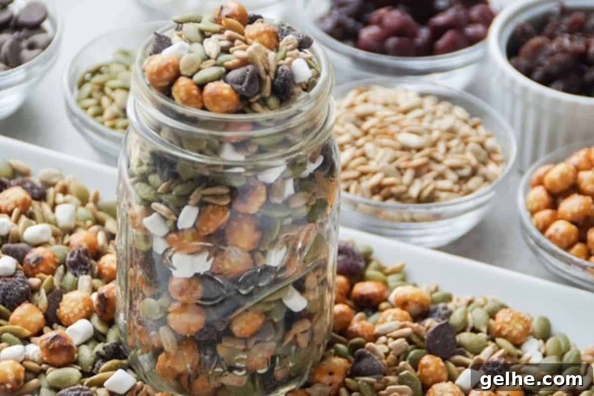 One glass mason jar filled with nut-free trail mix surrounded by trail mix on a white plate at its base. Ingredients in separate small glass bowls lined up to the side of the white plate.