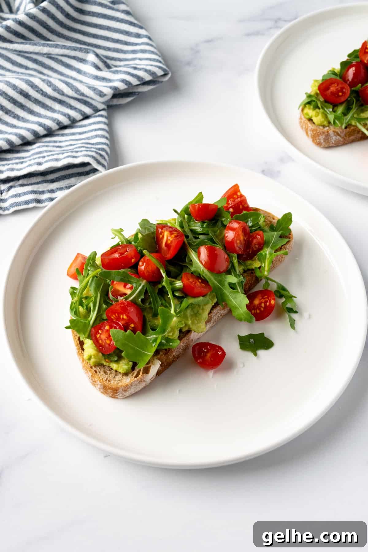 Tomato Avocado Toast with Arugula on a white plate.