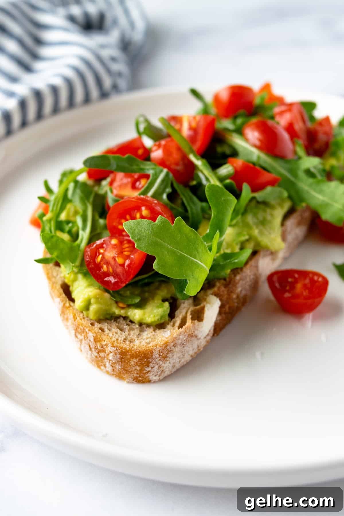 Tomato Avocado Toast with Arugula on a white plate.