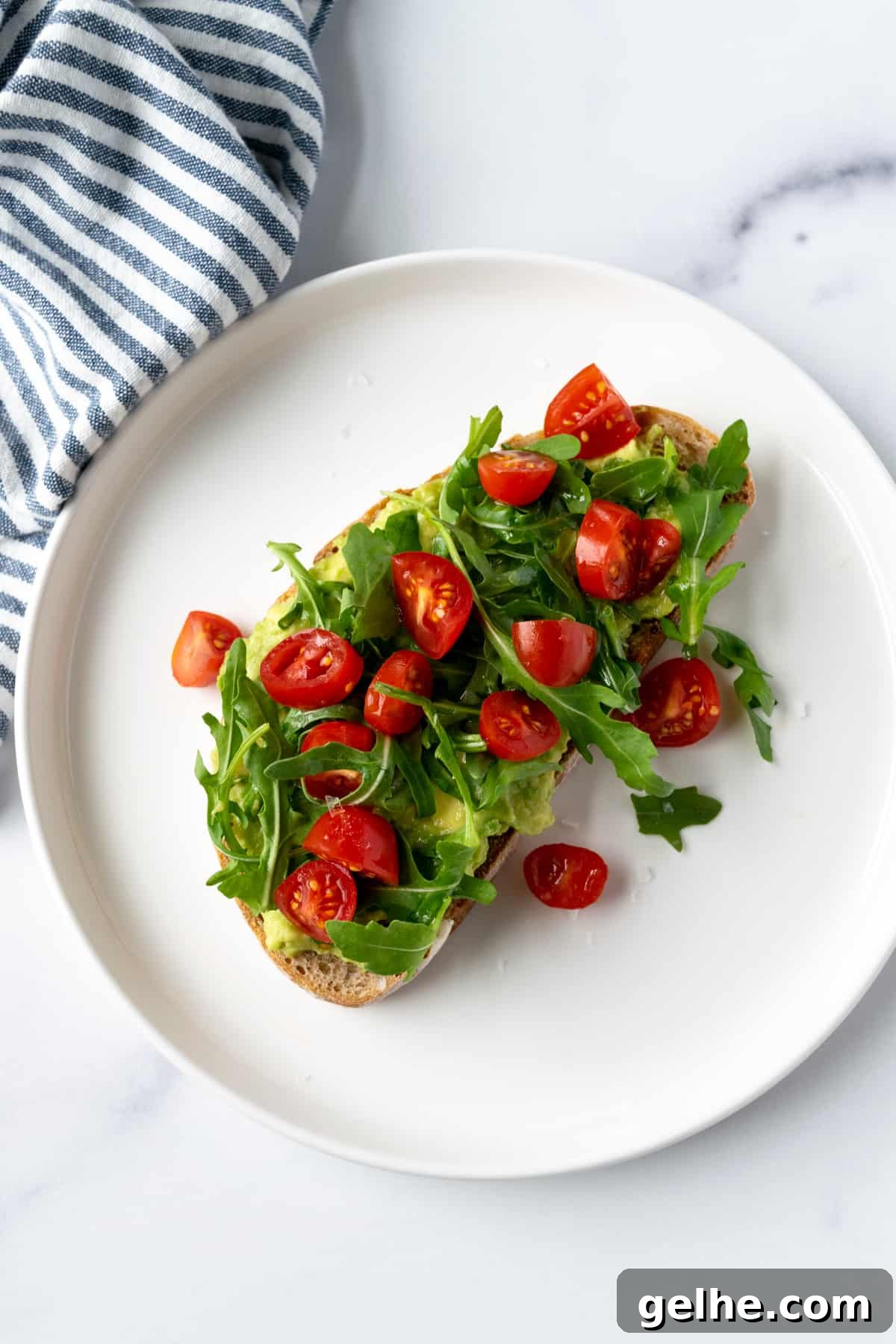 Tomato Avocado Toast with Arugula on a white plate.
