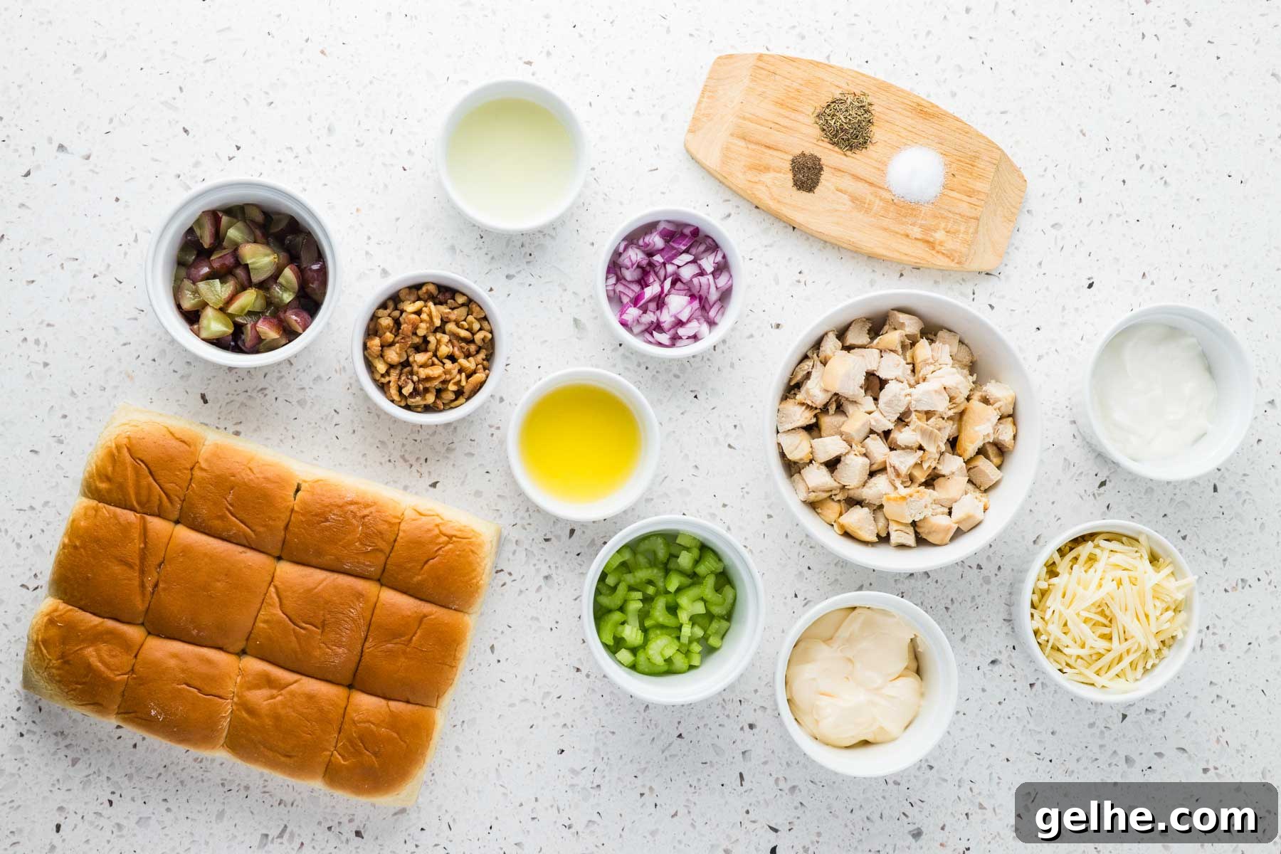 Ingredients for chicken salad sliders arranged on a countertop, including slider rolls, chicken, grapes, walnuts, celery, onion, cheese, mayonnaise, sour cream, oil, lemon juice, and seasonings.
