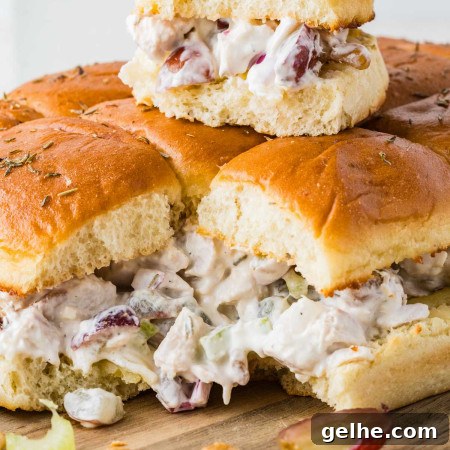 Close up of chicken salad sliders on Hawaiian rolls with grapes, celery, walnuts, and thyme on a wooden board.