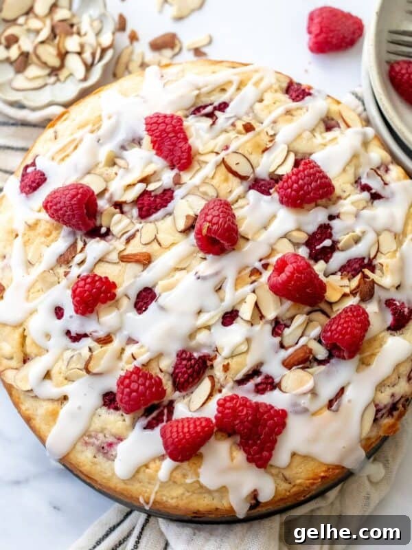 Raspberry Almond Cake on a white counter with raspberries and icing and forks to the side.