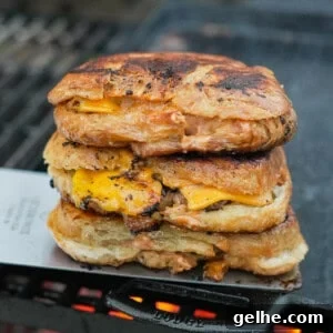 A stack of croissant three smashburgers on a cast iron skillet over the grill