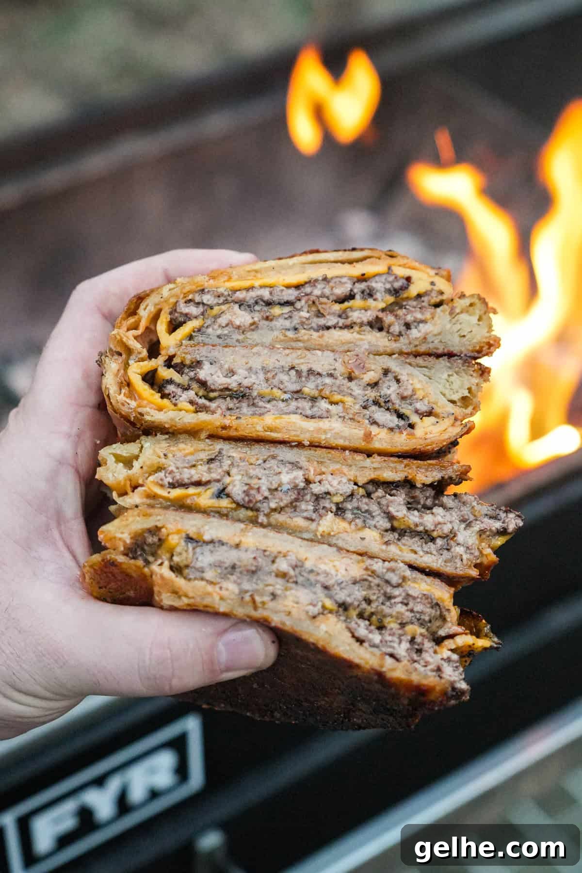 Two sliced croissant smashburgers with cheese, burger sauce and garlic butter with the grill fire in the background