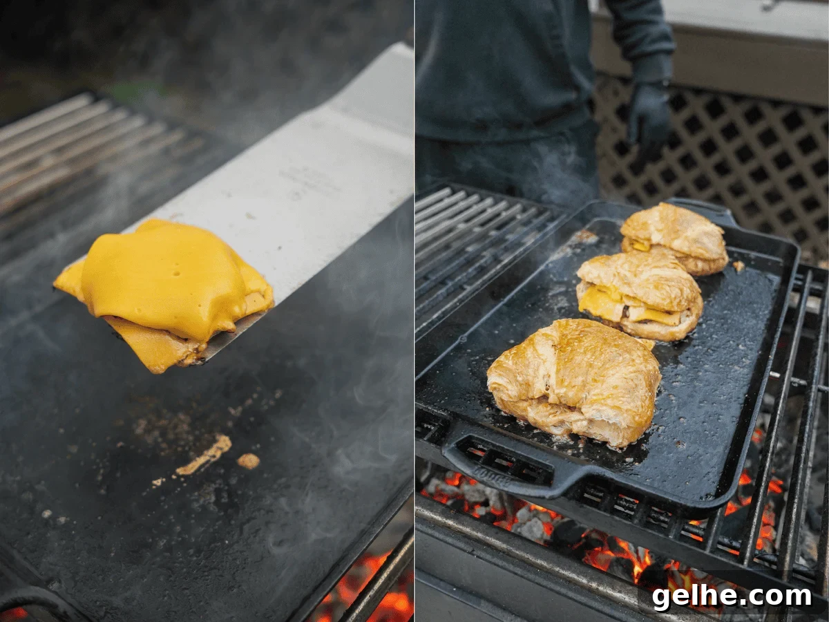 Slices of American cheese on a metal spatula over the grill and croissants ready for smashing on a cast iron skillet on the grill