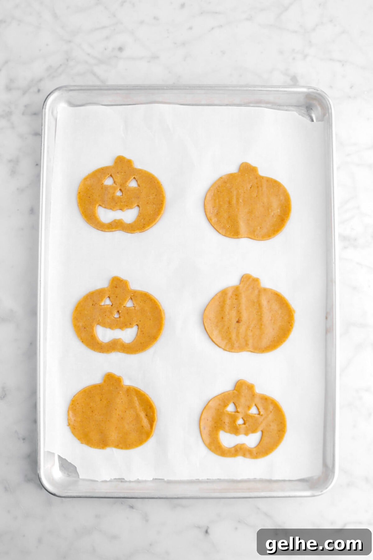 three jack o'lantern cookies with three pumpkin cookies on lined sheet pan.