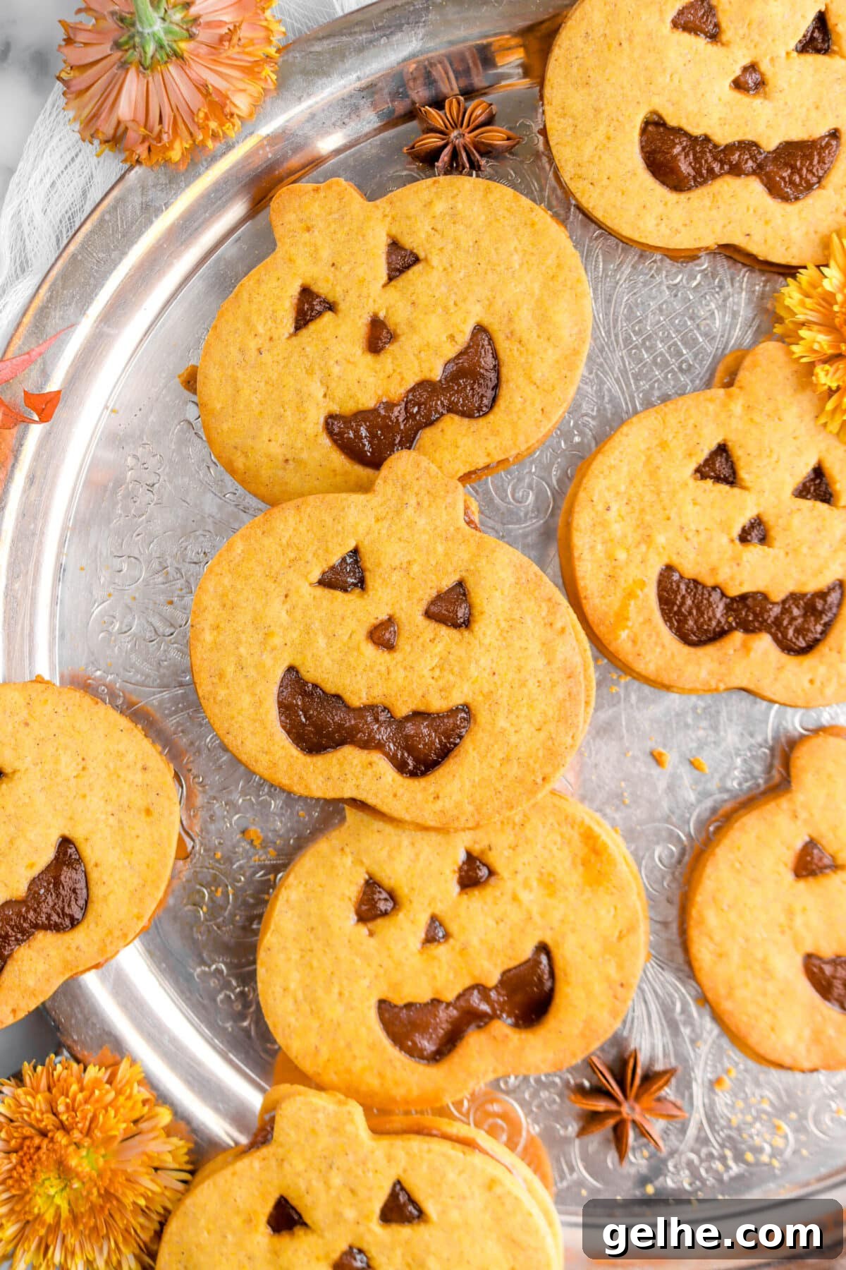 overhead close up of jack o'lantern sandwich cookies on silver tray with two star anise pods and mums around.