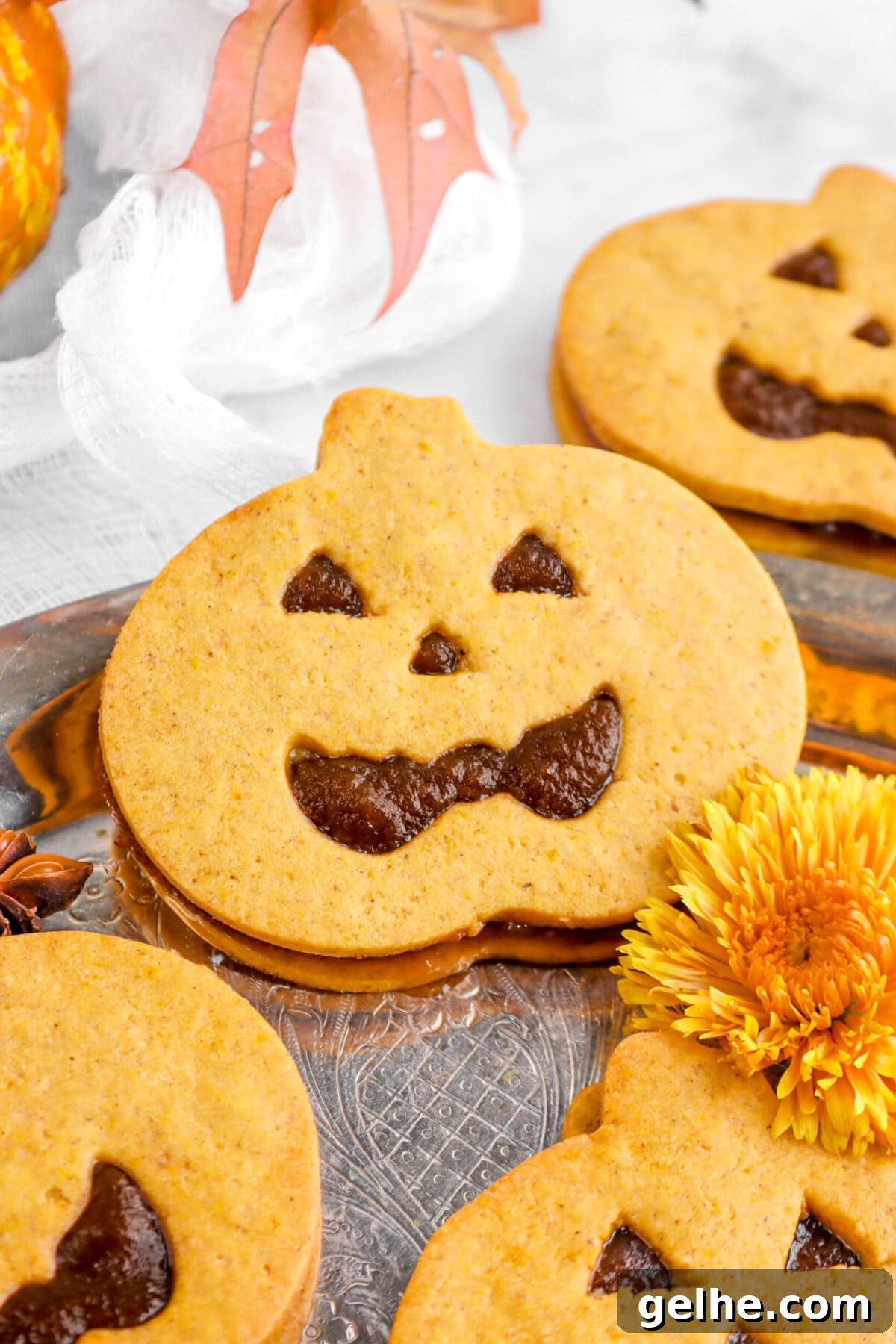 close up of a jack o'lantern sandwich cookie with yellow chrysanthemum beside.