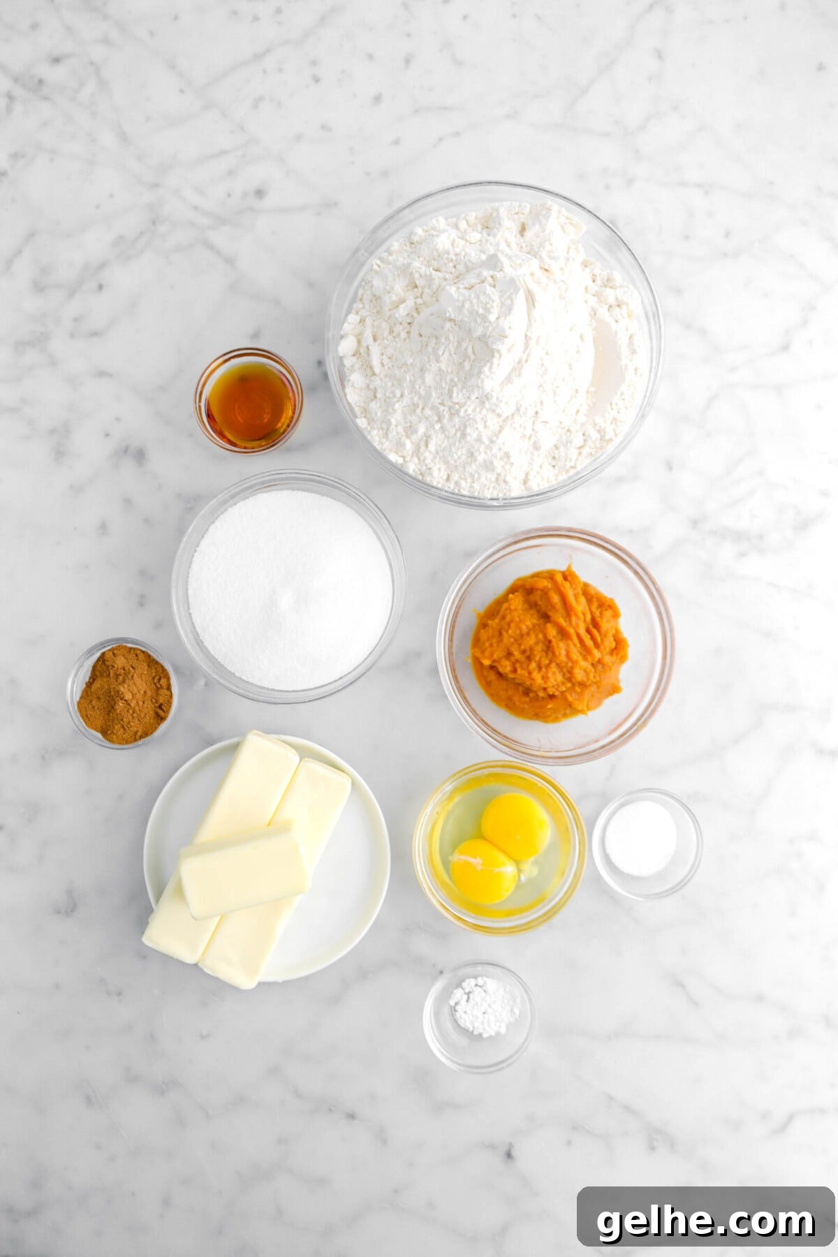 vanilla, flour, sugar, baking powder, pumpkin pie spice, pumpkin puree, eggs, butter, and salt on marble surface.