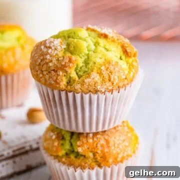 Two bakery style pistachio muffins stacked on a counter.