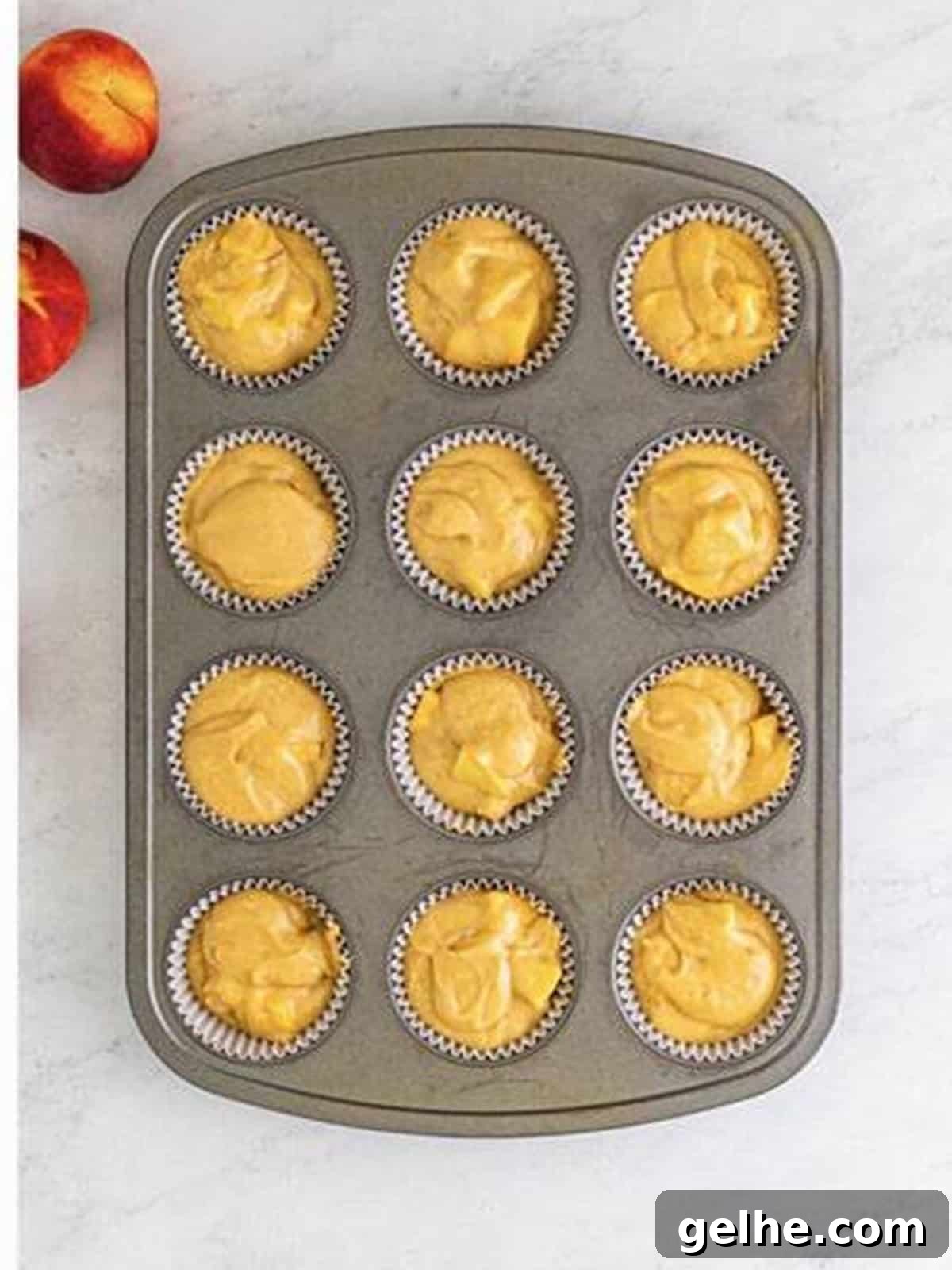 Peach muffin batter divided into a lined muffin tin.