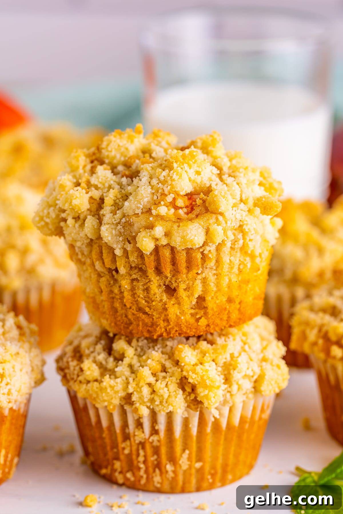 Stacked peach streusel muffins next to a glass of milk.