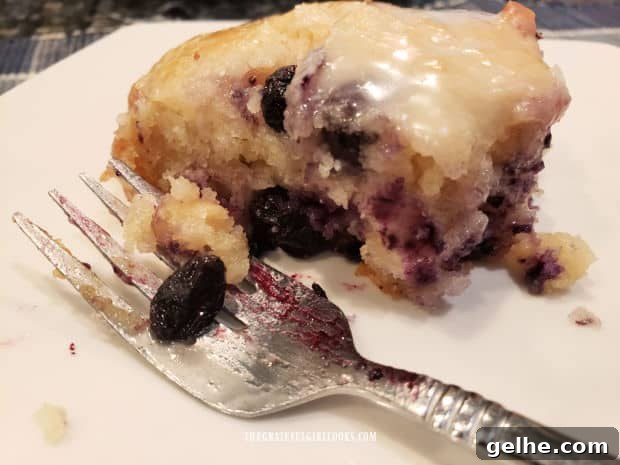 A fork and one of the vanilla glazed blueberry biscuits, on a white plate.