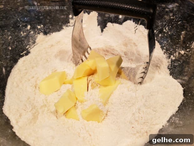 Cold butter is cut into the dry biscuit ingredients in a bowl.