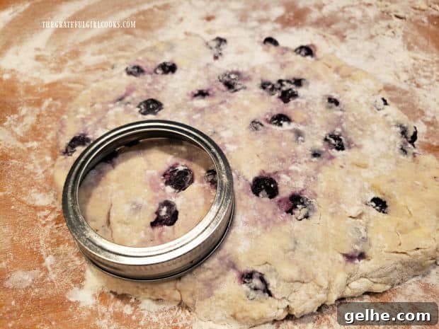 A small canning jar lid is used to cut out 8 blueberry biscuits from the dough.