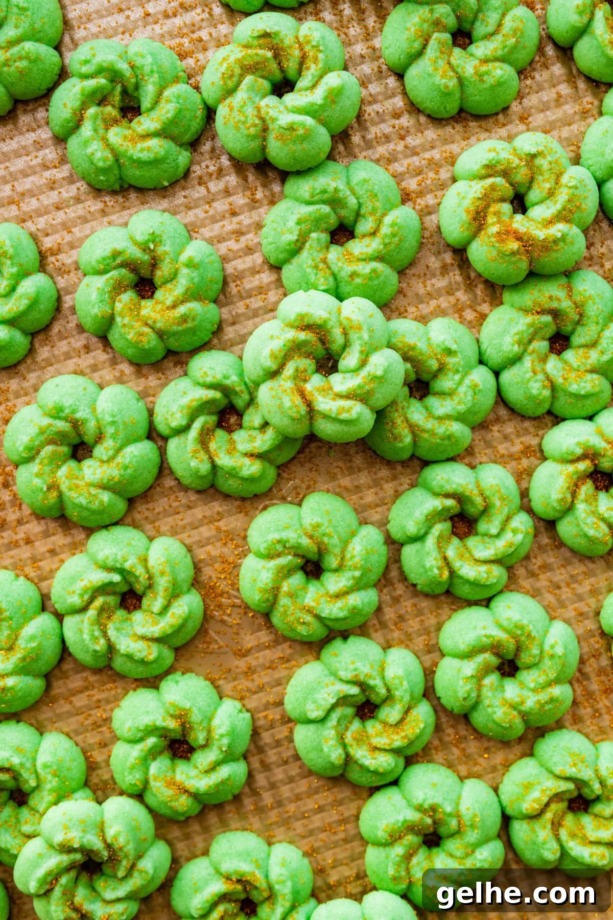 How to make Spritz cookies step-by-step: baked cookies on a baking sheet. Green Christmas wreathes with gold sprinkles.