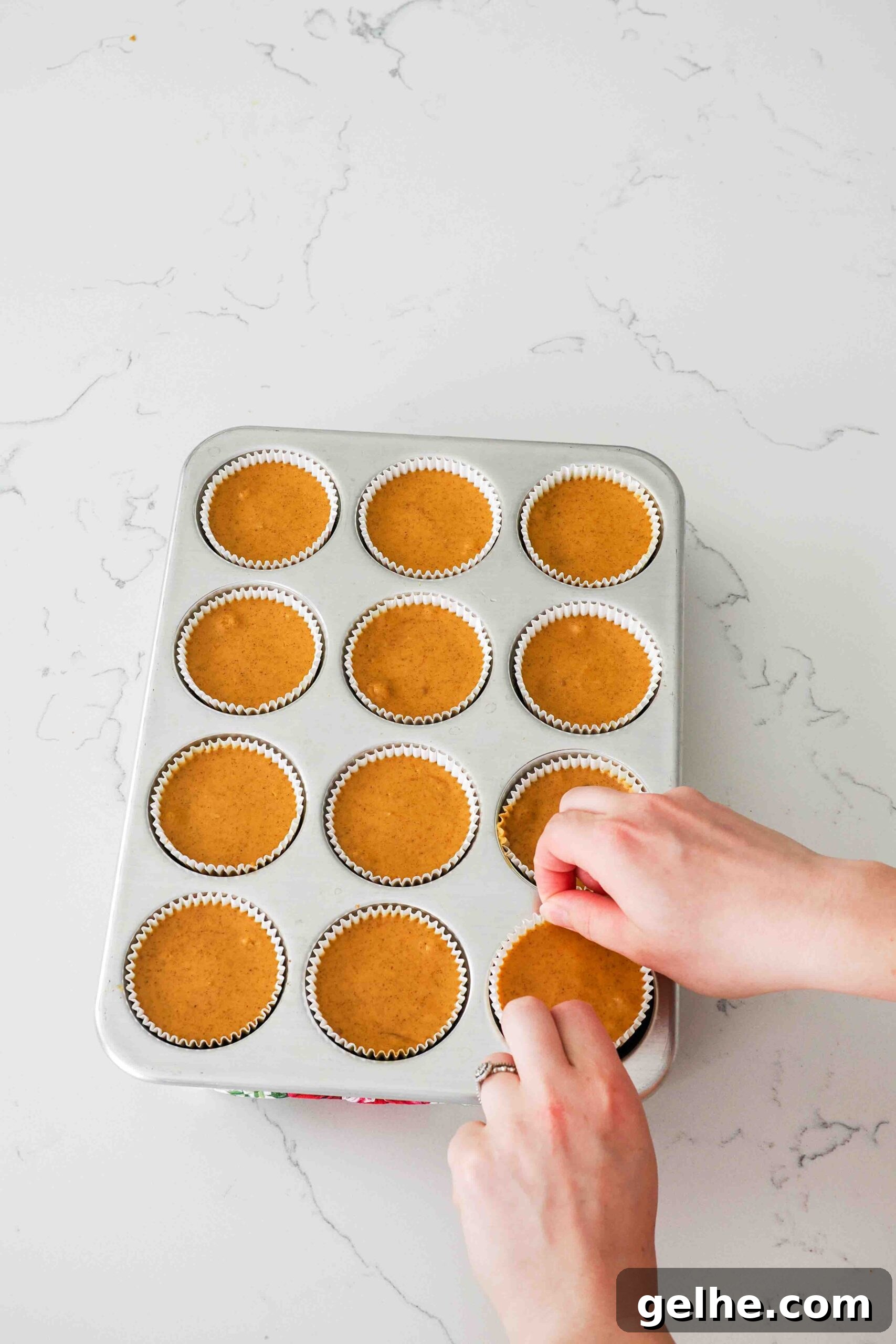 Mini Pumpkin Cheesecake Bites: Creamy Fall Dessert Recipe 14 Two hands pinch the liner of a mini cheesecake to remove it from a muffin pan.