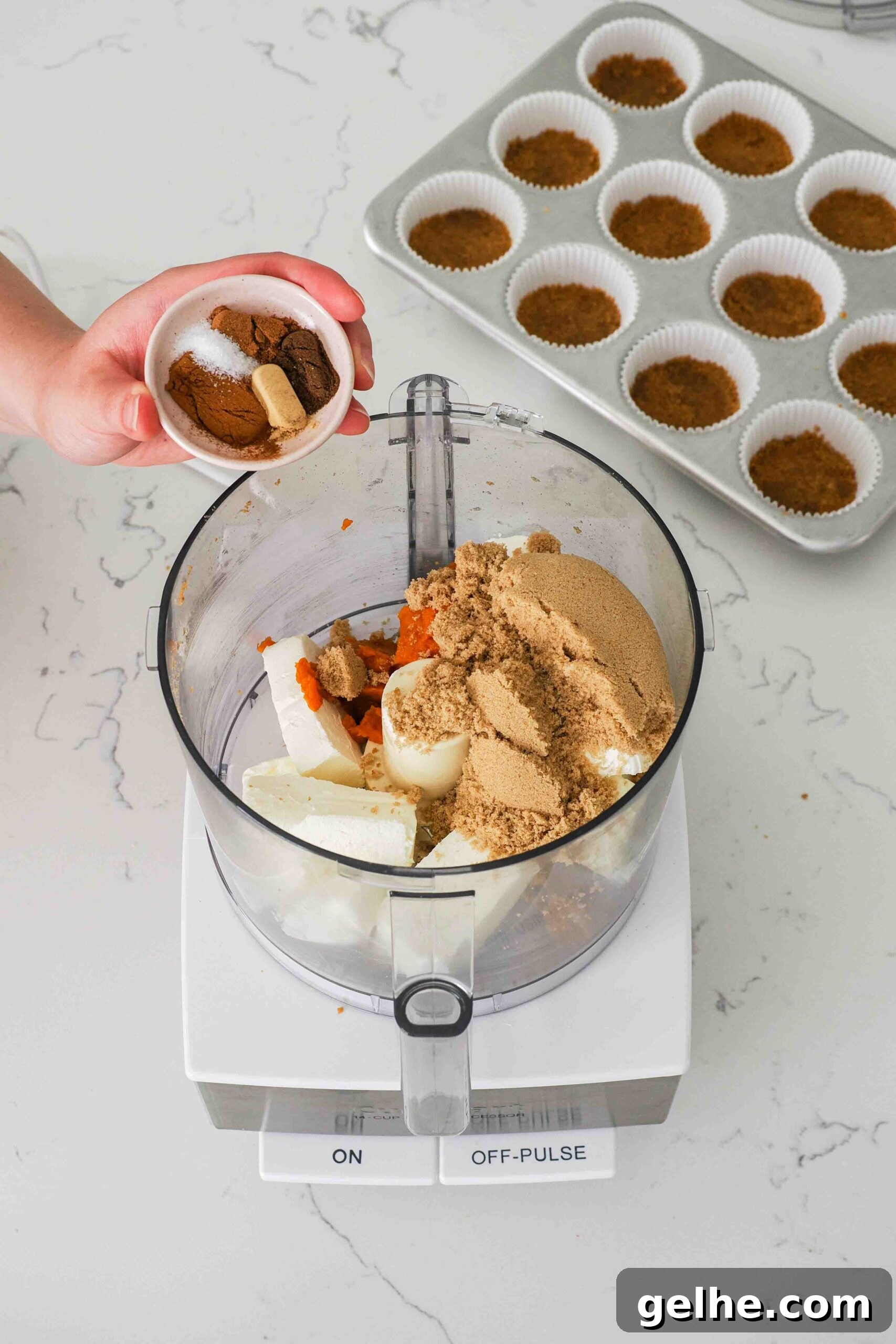 Mini Pumpkin Cheesecake Bites: Creamy Fall Dessert Recipe 7 A hand adds spices into a food processor bowl with cream cheese, pumpkin, and brown sugar.