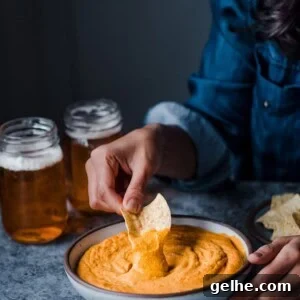 dipping tortilla chip into a bowl of cheesy buffalo cauliflower dip