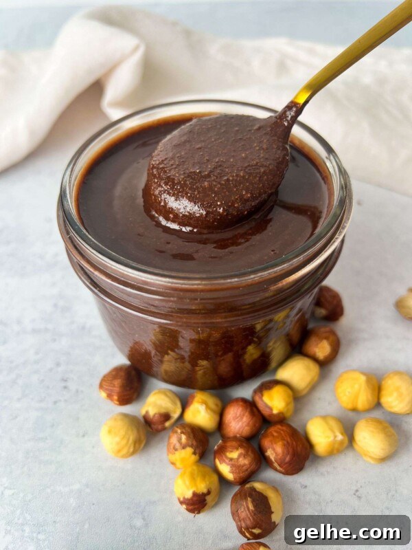 A glass jar filled with homemade Nutella chocolate hazelnut spread, with a spoon dipped in it.