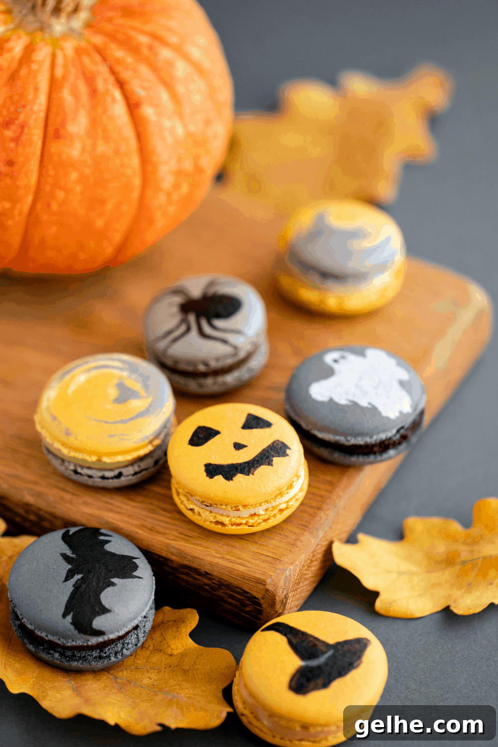 A wooden board with Halloween-themed macarons, including Jack-O-Lantern Macarons, ghosts, bats, and spiders, perfect for a festive Halloween treat.