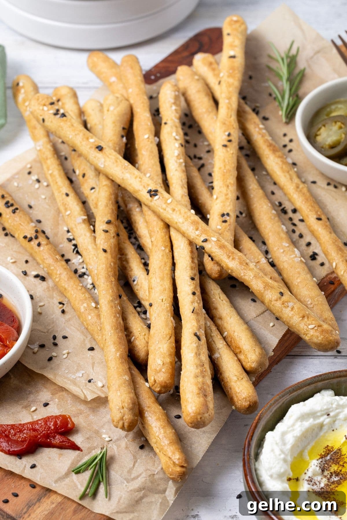 Crispy Sourdough Grissini Breadsticks for Snacking and Dipping 3 A close up photo of sourdough grissini garnished with black and white sesame seeds. The crunchy sourdough breadsticks are piled on a board surrounded by some antipasto type food.