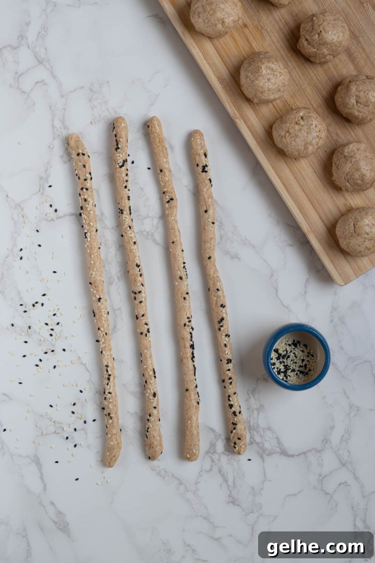 Crispy Sourdough Grissini Breadsticks for Snacking and Dipping 5 A photo showing how to roll the small bowls of dough into long dough strips, rolled in sesame seeds.