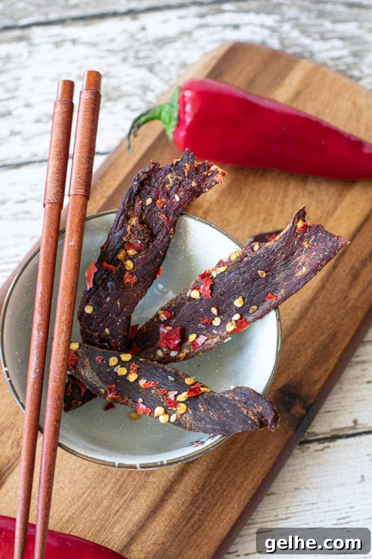 venison jerky in bowl atop a cutting board with chop sticks and Fresno chili