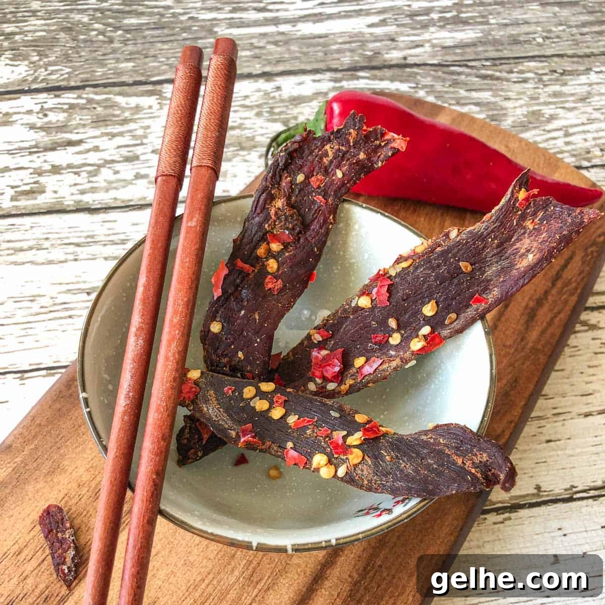 Venison jerky in bowl with chop sticks on cutting board